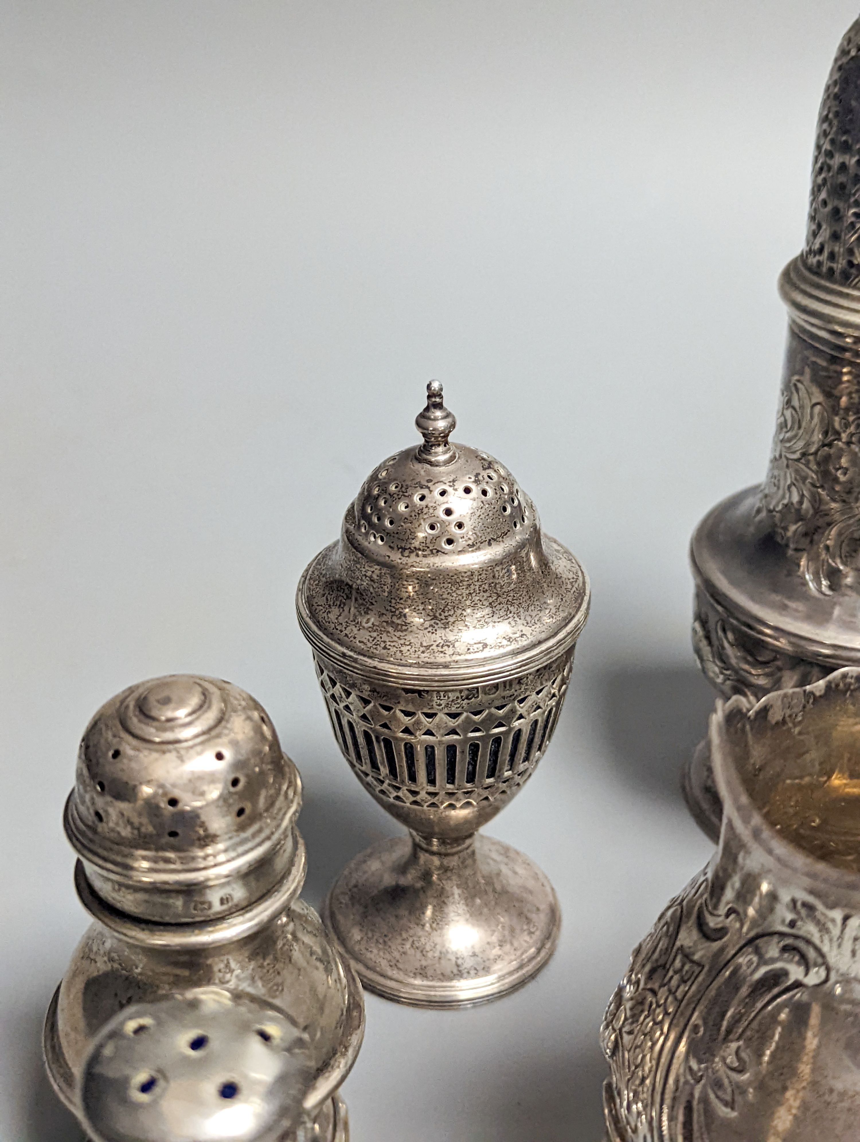 A Victorian embossed silver cream jug, London, 1883, 92mm, two 18th century silver pepperettes, one with plated cover, four later condiments (two silver), a silver spoon and small 800 standard photograph frame.